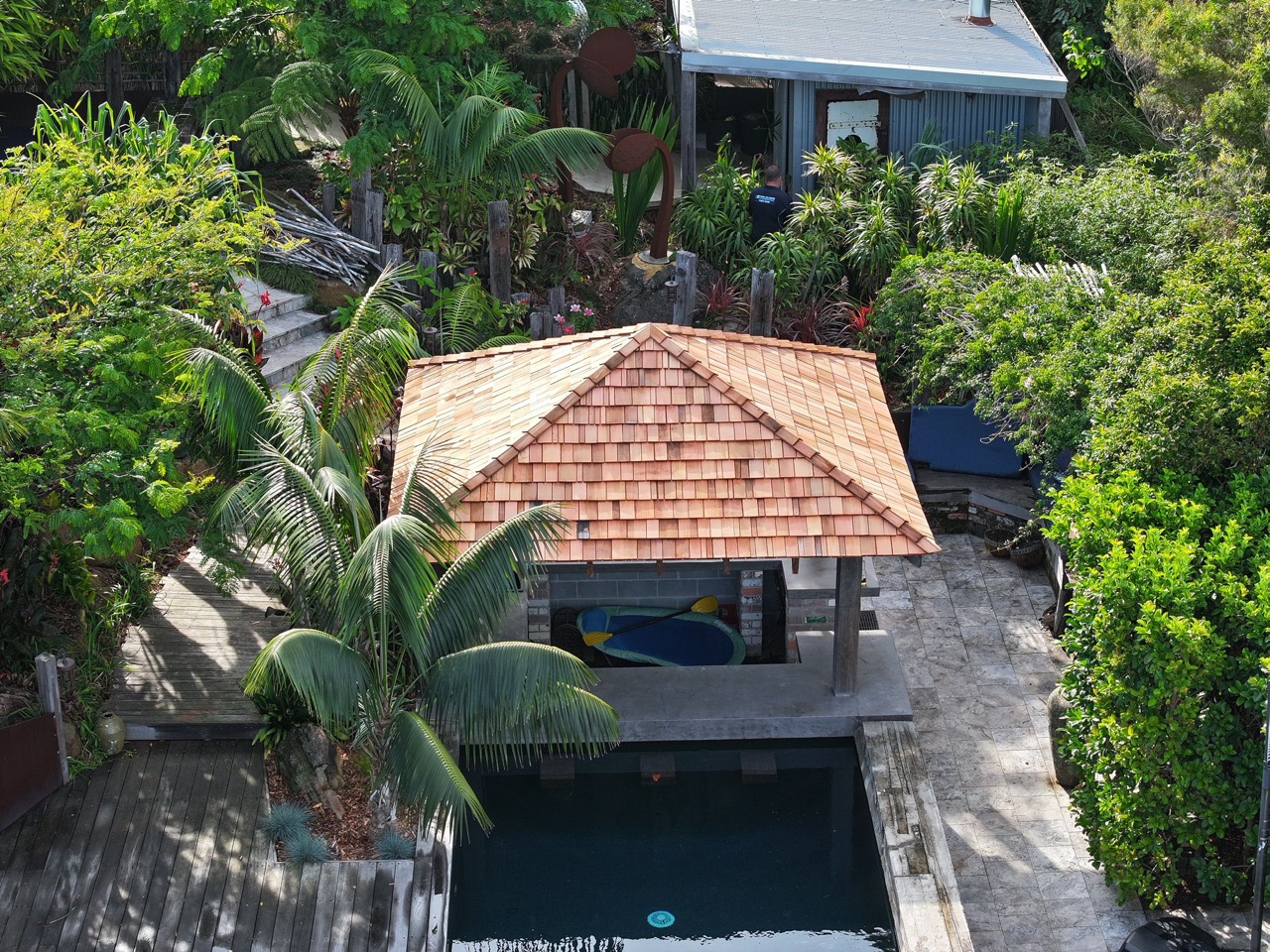 Aerial view of a cedar-roofed Bali hut beside a pool, framed by palms